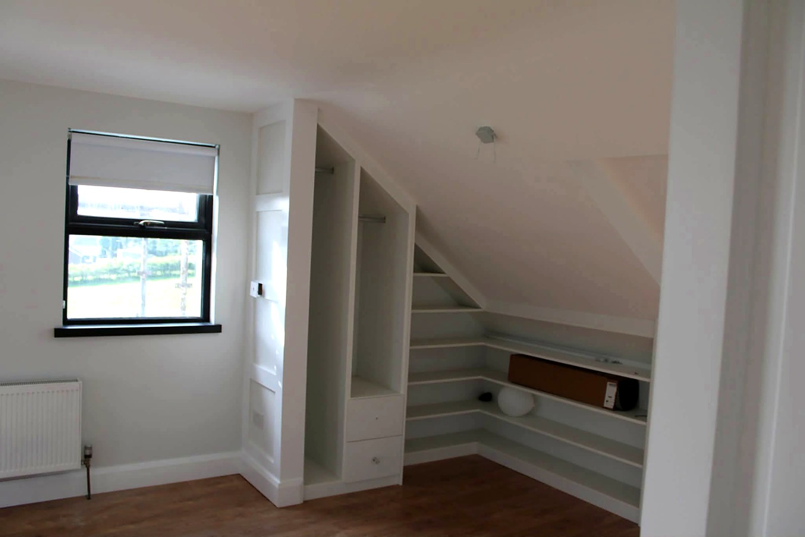 Attic bedroom with fitted wardrobes and shelving painted to match the walls