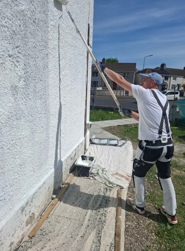 Painter rolling a fresh white masonry coat onto an exterior rendered wall