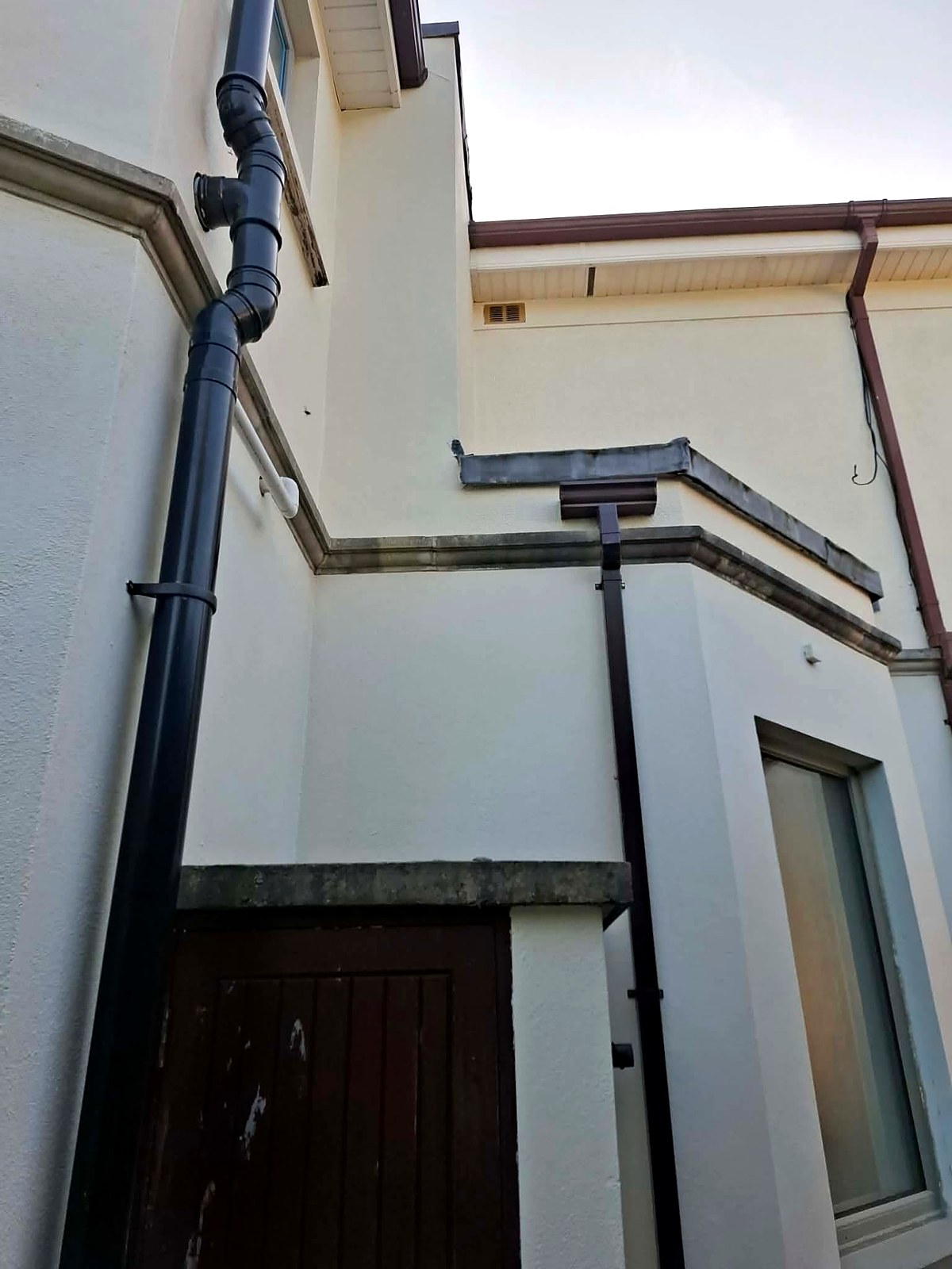 Close-up of painted gutters, hopper heads and downpipes shedding water away from the render